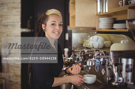 Portrait of smiling waitress preparing a cup of coffee in cafe