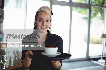 Portrait of waitress standing with cup of coffee in cafe