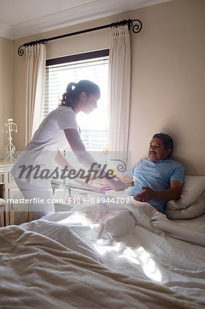 Doctor serving breakfast to senior patient in bedroom