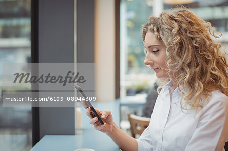 Woman using mobile phone at counter in cafeteria