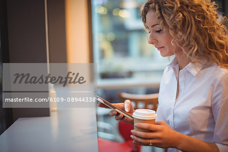 Woman using mobile phone while having coffee at counter in cafeteria