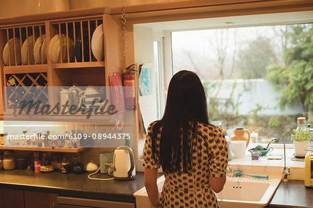 Rear view of woman looking through window in kitchen at home