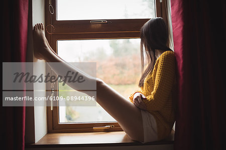 Woman sitting at window sill and looking outside at home