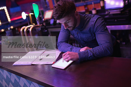 Bartender using digital tablet at counter in bar