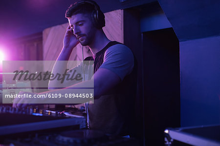Male dj listening to headphones while playing music in bar Male dj listening to headphones while playing music in bar