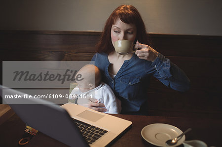 Mother having coffee while holding her baby in café