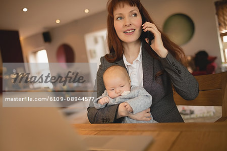 Mother talking on mobile phone while holding her baby at home