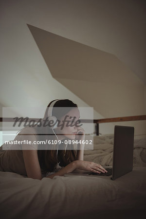 Woman with headphones using laptop on bed at home