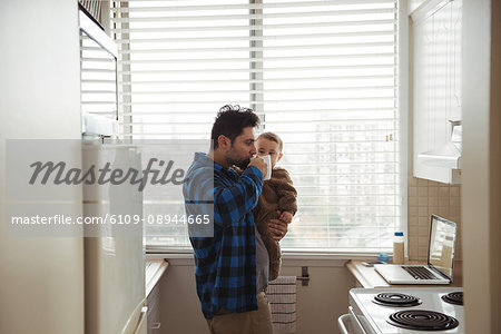 Father having coffee while holding his baby in kitchen