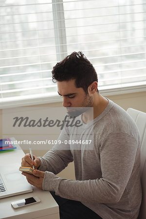 Handsome man writing on sticky note at home