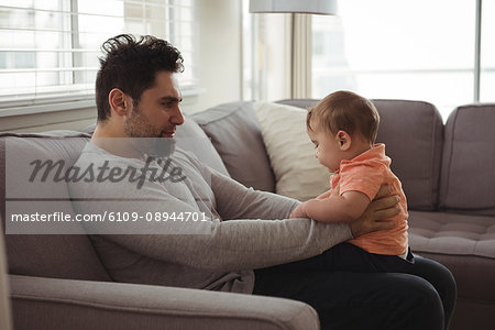 Father playing with his baby on sofa in living room at home