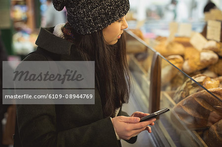 Woman using her mobile phone near the bakery counter in the supermarket