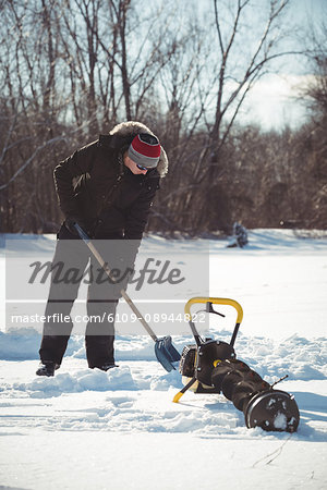 Ice fisherman digging with shovel in snowy landscape
