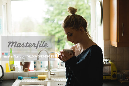 Thoughtful woman holding a coffee cup in kitchen at home