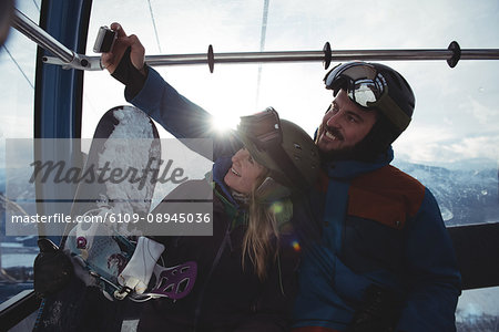 Happy couple taking selfie in overhead cable car against sky during winter