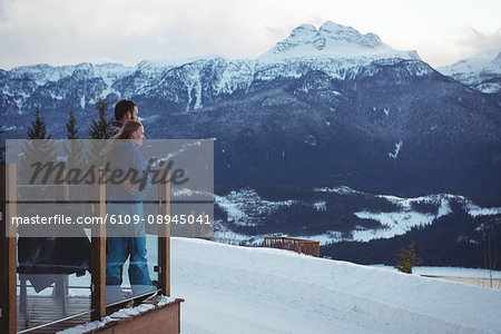 Couple embracing while standing by railing against snowcapped mountains