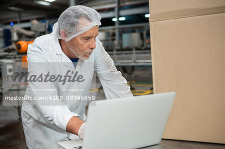 Serious male worker using laptop in cold drink factory