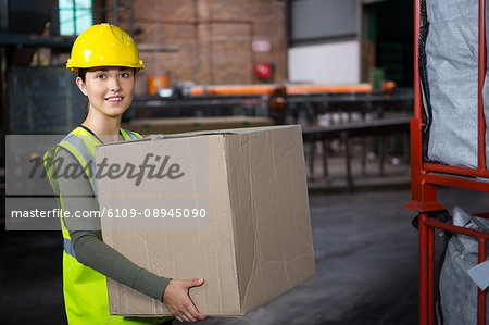 Portrait of beautiful female worker carrying box in warehouse