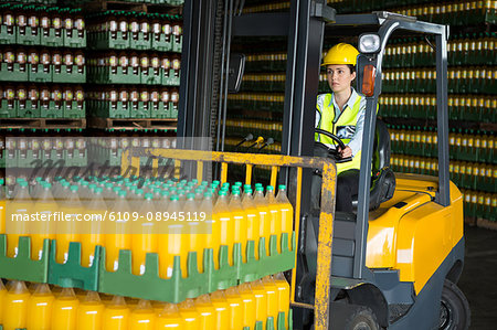 Confident female worker driving forklift in distribution warehouse