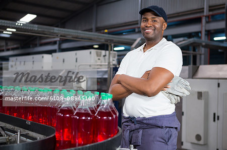 Portrait of male worker with arms crossed standing by bottles on production line in factory