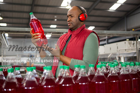 Serious male worker wearing protective earwear while inspecting bottle in factory