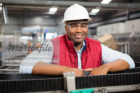 Portrait of smiling male employee standing by conveyor belt in factory