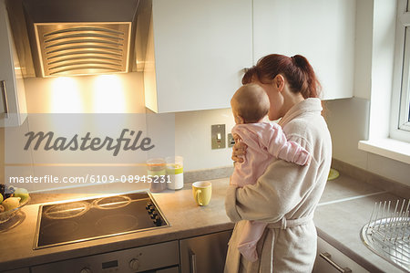 Loving mother carrying baby in kitchen