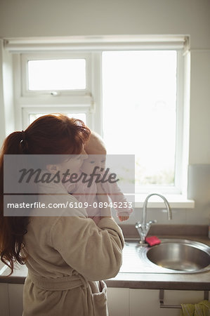 Loving mother kissing baby in kitchen at home