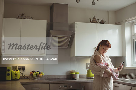 Mother with baby and mobile phone in domestic kitchen