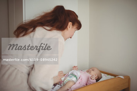 Loving mother changing babys diaper in crib at home