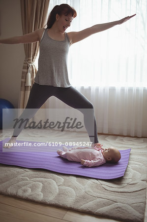 Happy mother doing warrior pose while looking at baby in house