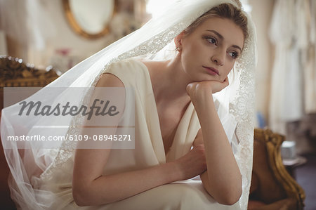 Thoughtful young bride in a white dress sitting on sofa in boutique Thoughtful young bride in a white dress sitting on sofa in boutique