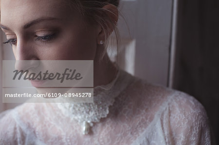 Thoughtful young bride standing near window in a boutique