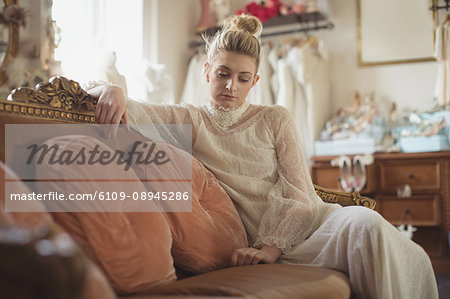 Thoughtful young bride in a white dress sitting on sofa in a boutique