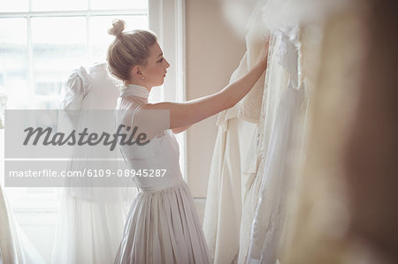 Young bride selecting wedding dress from clothes hanger in a boutique Young bride selecting wedding dress from clothes hanger in a boutique