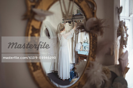 Reflection of bride selecting wedding dress from clothes hanger in the mirror at boutique