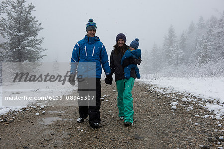 Full length of happy parents with son walking on road during winter