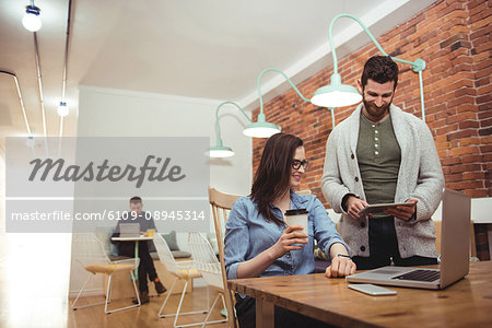 Male and female executives discussing over digital tablet at desk in office