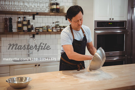 Male chef emptying flour on counter top at restaurant