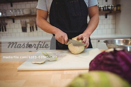 Midsection of male chef cutting cabbage on cutting board in commercial kitchen