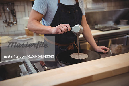 Midsection of male chef pouring pancake mixture on frying pan in commercial kitchen