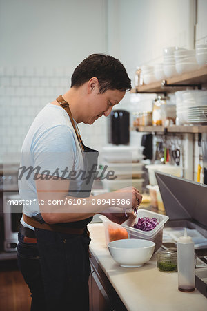 Side view of male chef adding chopped cabbage into bowl in commercial kitchen