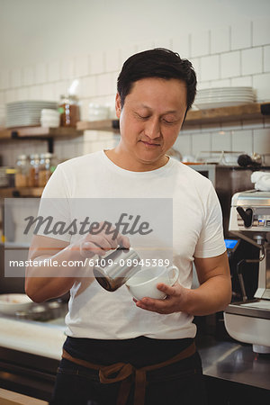 Male barista pouring milk into coffee cup at cafe