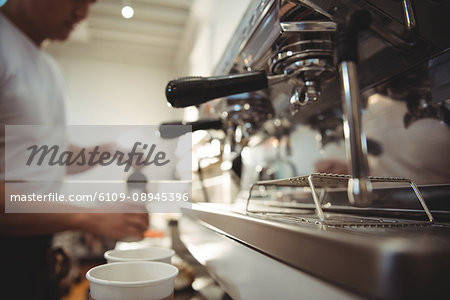 Close-up of coffee machine with barista working in background at cafe