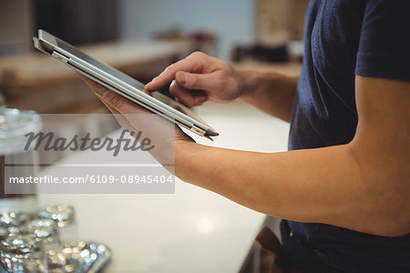 Midsection side view of barista using digital tablet in coffee shop