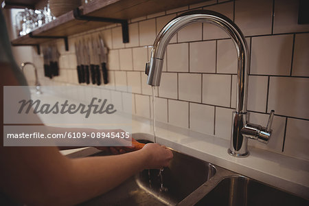 Close-up of female chef washing carrot under the tap in commercial kitche