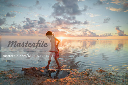 Girl wading in ocean surf on tranquil sunset beach