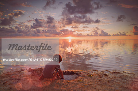 Boy playing in wet sand on tranquil sunset beach Boy playing in wet sand on tranquil sunset beach