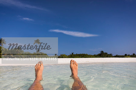 Personal perspective barefoot man floating in tropical ocean surf with view of beach