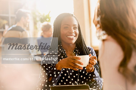 Smiling women friends drinking coffee and talking in cafe